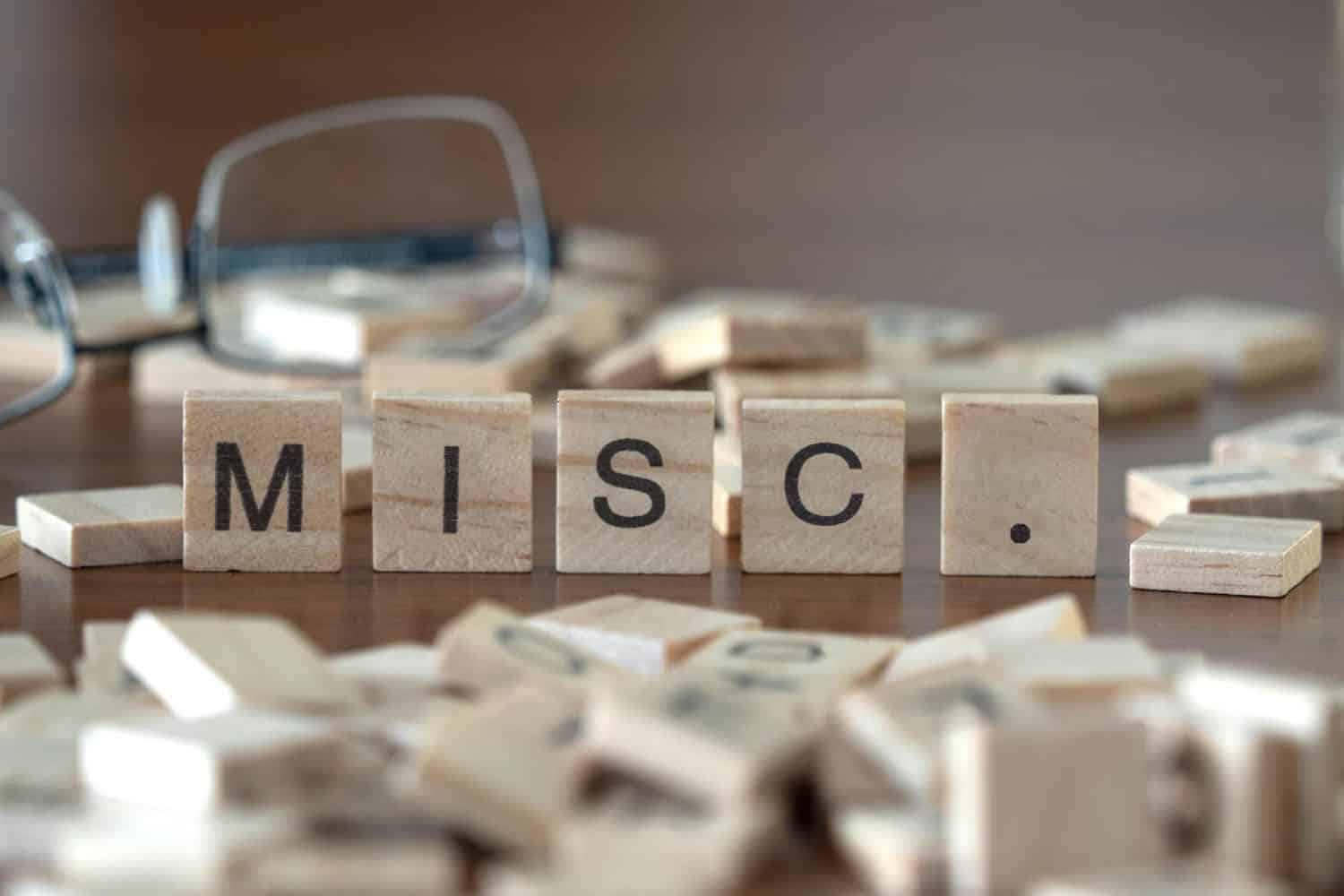 the acronym misc. for miscellaneous word or concept represented by wooden letter tiles on a wooden table with glasses and a book